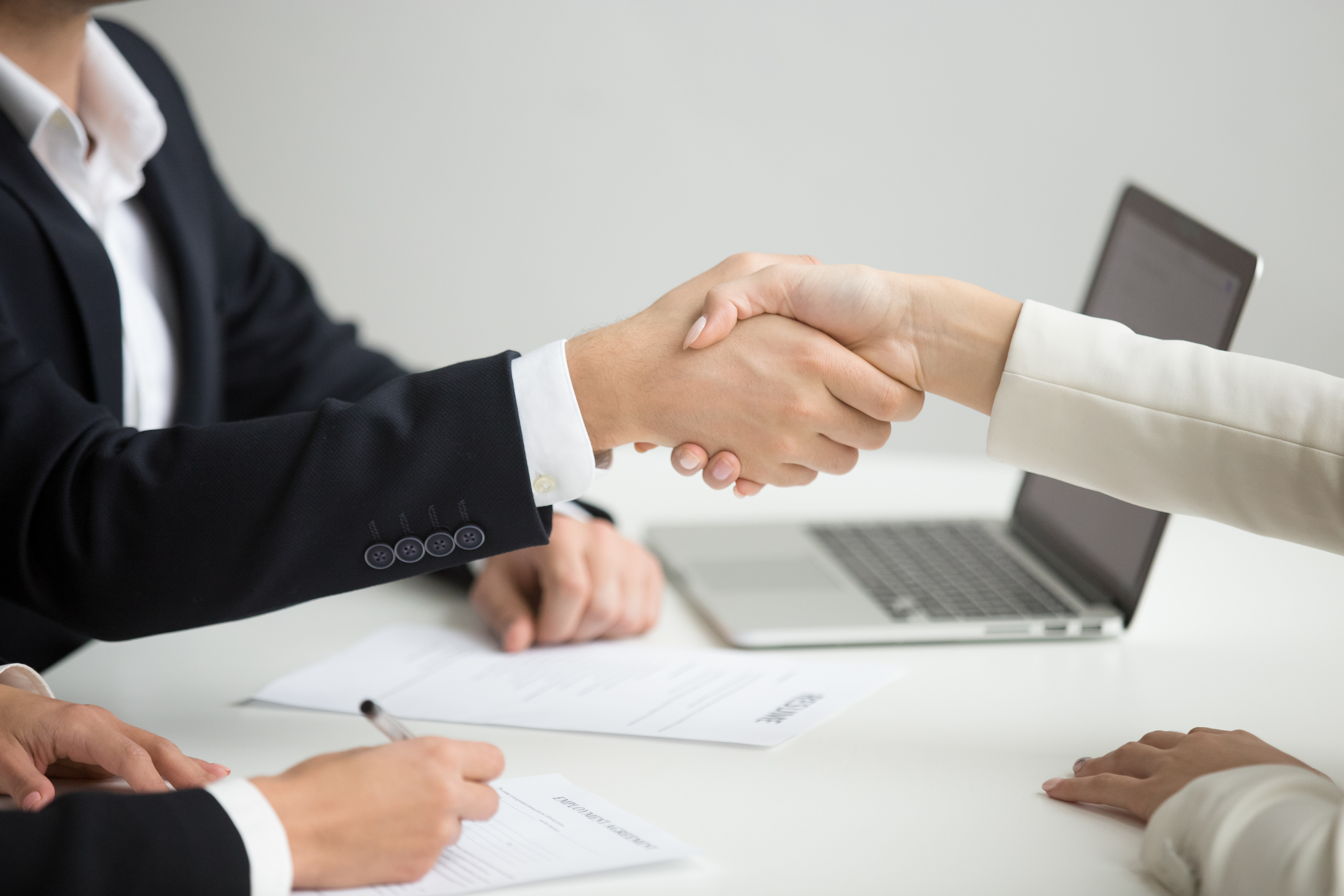 Zwei Personen in Business-Kleidung schütteln sich die Hände, Fokus auf dem Handschlag als Ausdruck von Vertrauen und persönlicher Verbindung im Recruiting.