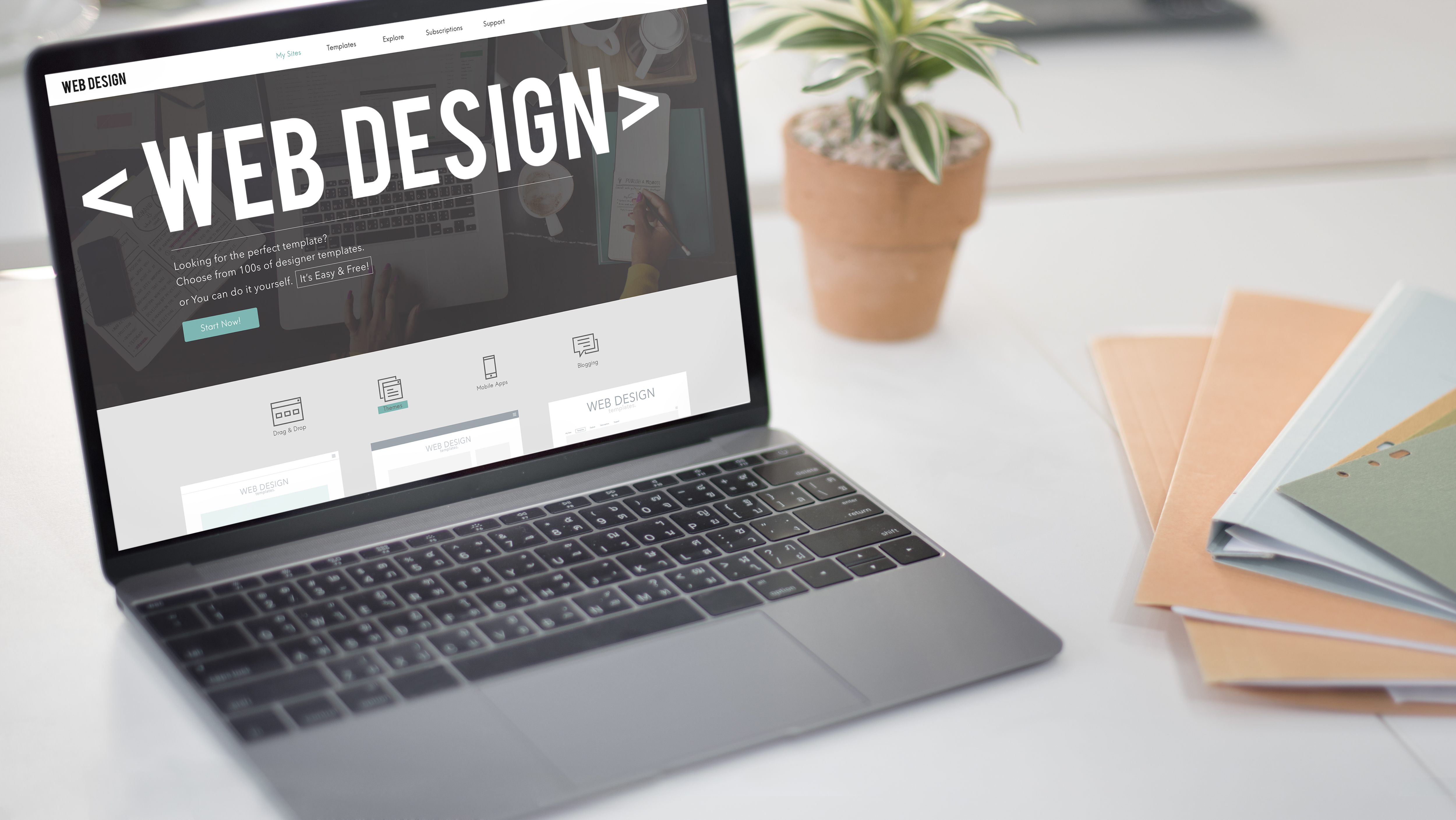 Offener grauer Laptop auf weißem Tisch, auf dem eine Website angezeigt wird mit dem Titel Web Design, umgeben von Mappen und kleiner Pflanze.